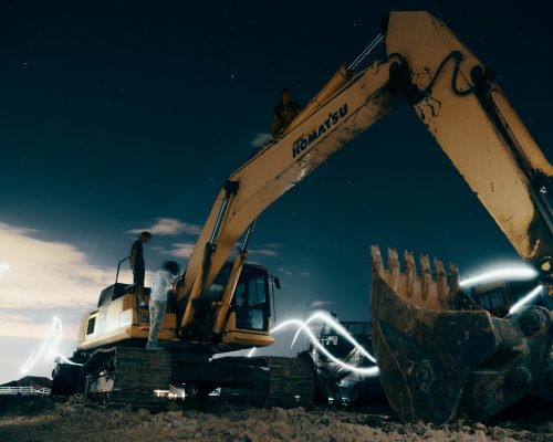 pexels-photo-2449603-2449603 A powerful excavator at a construction site under the night sky, with workers around.
