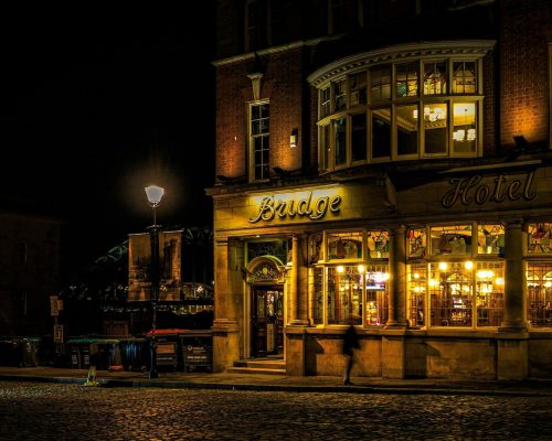 pexels-photo-8409922-8409922 Bridge Hotel in Newcastle upon Tyne illuminated at night, capturing vibrant city life.